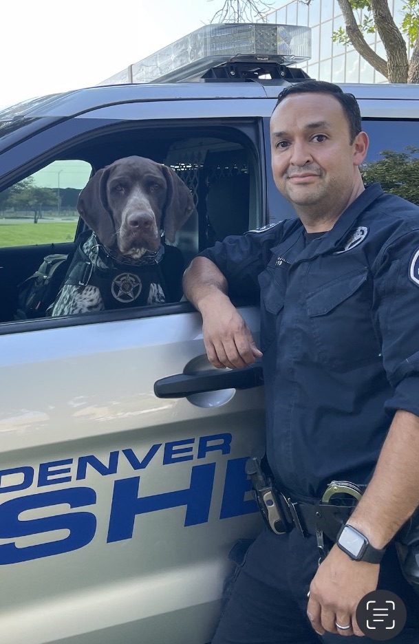 Handler standing beside a patrol vehicle with a working dog.